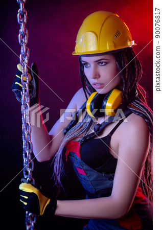 a construction girl in a hard hat and overalls with a long chain in her hands a construction girl in a hard hat and overalls with a long chain in her hands 90076817