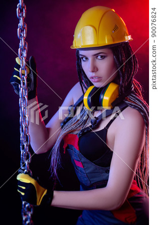 a construction girl in a hard hat and overalls with a long chain in her hands a construction girl in a hard hat and overalls with a long chain in her hands 90076824