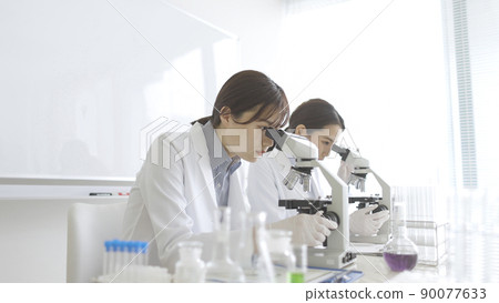 A woman in a white coat looking through a microscope A woman in a white coat looking through a microscope 90077633