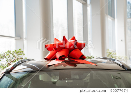 a red gift bow on the roof of a new car in the car dealership. a red gift bow on the roof of a new car in the car dealership. 90077674