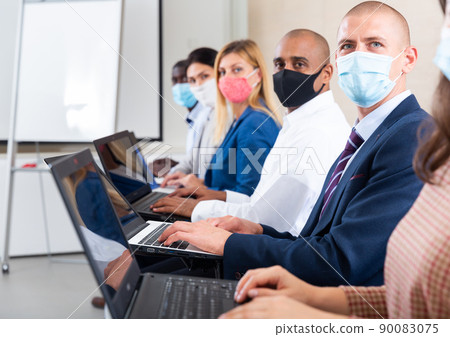 Side view of man in mask working with laptop during business training Side view of man in mask working with laptop during business training 90083075