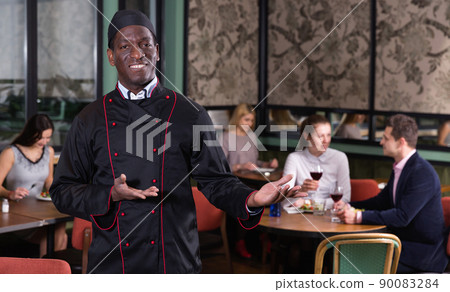 Smiling politely African American chef inviting to visit cozy restaurant 90083284
