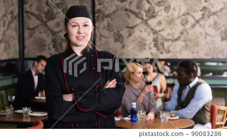 Confident professional female chef posing with arms crossed on background with restaurant guestsConfident professional female chef posing with arms crossed on background with restaurant guests Confident professional female chef posing with arms crossed on background with restaurant guestsConfident professional female chef posing with arms crossed on background with restaurant guests 90083286