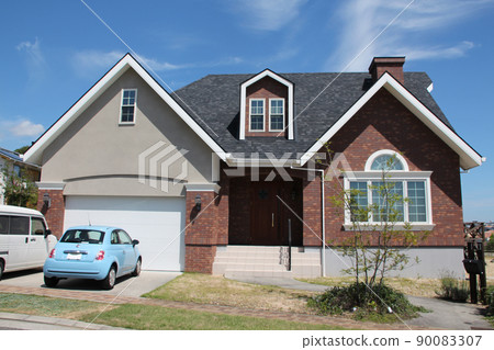 A fashionable and cute mansion with a large red brick gable roof with a dormer and a chimney in a North American style that shines in the blue sky A fashionable and cute mansion with a large red brick gable roof with a dormer and a chimney in a North American style that shines in the blue sky 90083307