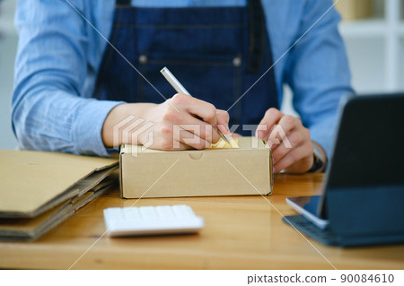Start up small business owner writing address on cardboard box a. 90084610