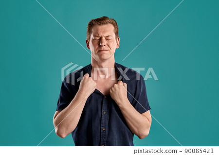 Close-up portrait of a ginger guy in navy t-shirt posing on blue background. Sincere emotions. 90085421