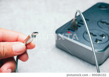 Human hand holding a type C mobile phone charger cable connected to a usb charging socket 90086102