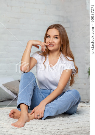 Indoor portrait of a beautiful blonde woman posing sitting on a bed. Indoor portrait of a beautiful blonde woman posing sitting on a bed. 90087272