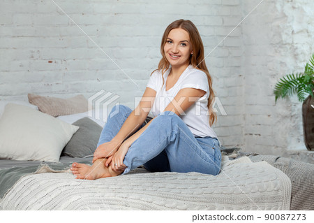 Indoor portrait of a beautiful blonde woman posing sitting on a bed. 90087273
