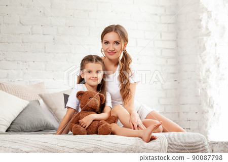 Indoor portrait of a beautiful mother with her charming little daughter posing against bedroom interior. 90087798