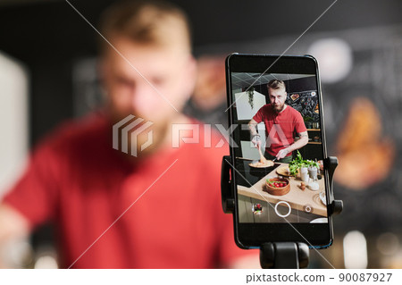 Selective focus shot of modern Caucasian food blogger cooking pasta filming process on smartphone camera 90087927