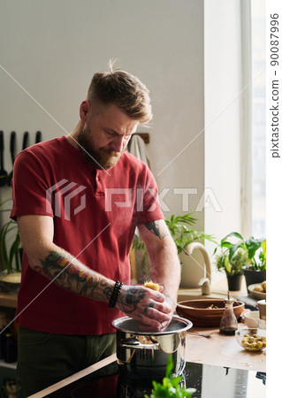 Modern Caucasian chef standing in loft kitchen at home putting spaghetti into pot with boiling water 90087996