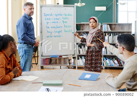 Group of multi-ethnic immigrant students learning English language at school doing task with irregular verbs together Group of multi-ethnic immigrant students learning English language at school doing task with irregular verbs together 90089002