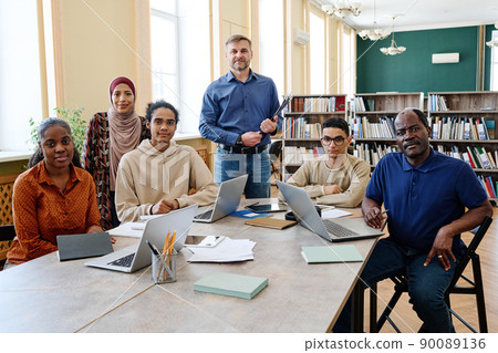 Group portrait of modern English language teacher and multi-ethnic immigrant students having class in library looking at camera 90089136