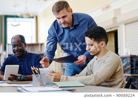 Mature Caucasian man working as English language teacher for immigrants explaining grammar rule to his student 90089224