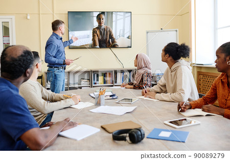 Group of multi-ethnic immigrant students sitting at table watching educational video during English class 90089279