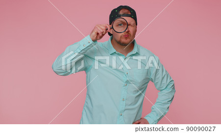 Investigator researcher man with magnifying glass near face, looking into camera with big zoom eye Investigator researcher man with magnifying glass near face, looking into camera with big zoom eye 90090027