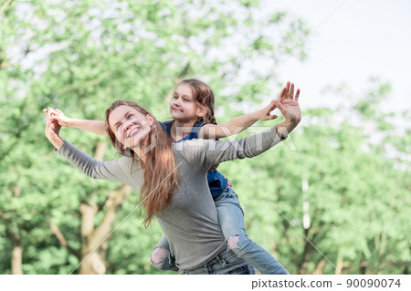 Cute young daughter on a piggy back ride with her mother 90090074
