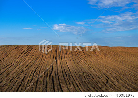 Newly ploughed agricultural field under cloudy blue sky 90091973