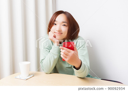 A woman sitting in a room and operating a smartphone 90092934