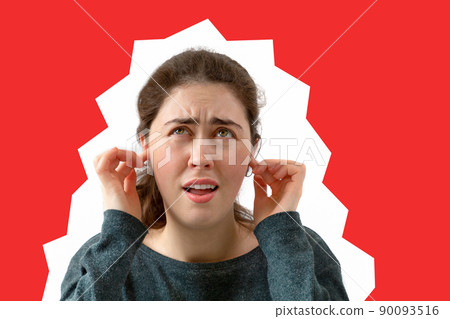 A young woman covers her ears from the noise. Emotion of discontent and irritation on the face. Red background. Copy space A young woman covers her ears from the noise. Emotion of discontent and irritation on the face. Red background. Copy space 90093516