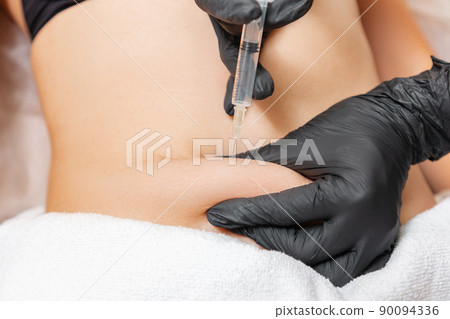 Liposuction. A doctor of aesthetic cosmetology makes lipolytic injections to burn body fat on a woman's belly. Close up. Professional cosmetology in a beauty salon 90094336