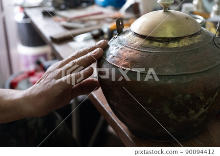 Restoration of an old jug of metal and other antiques, a man's hand touches the jug 90094412
