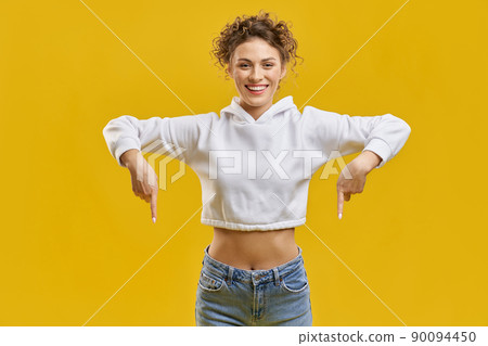 Front view of pretty woman showing down, pointing by fingers. Attractive girl standing, smiling, looking at camera, wearing white khudi and blue jeans. Concept of modern life. Front view of pretty woman showing down, pointing by fingers. Attractive girl standing, smiling, looking at camera, wearing white khudi and blue jeans. Concept of modern life. 90094450