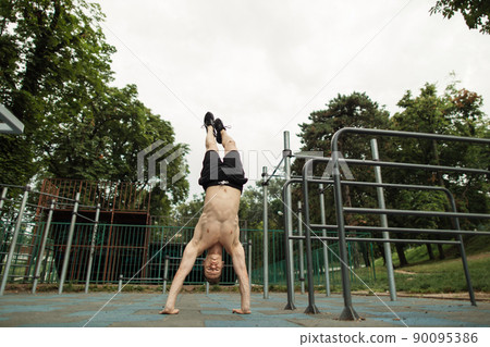 Shirtless man doing a handstand on the outdoor gym. Shirtless man doing a handstand on the outdoor gym. 90095386