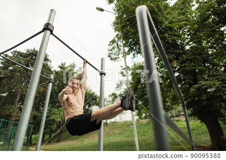 Strong shirtless caucasian athlete performing corner on horizontal bar Strong shirtless caucasian athlete performing corner on horizontal bar 90095388