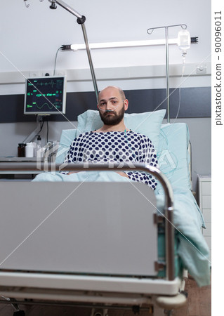 Depressed male with chronic bronchitis treated with saline for hydration from iv drip line connected to monitor measuring vitals. Patient in hospital bed recieving intravenous treatment. 90096011