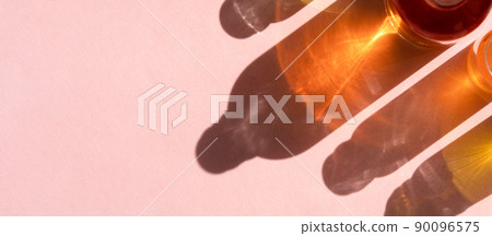 Different cosmetic glass bottles standing on beige background. Abstract pattern by shadows and illuminating reflections in the sunlight. Red, green and yellow shades. Flat lay style with copy space Different cosmetic glass bottles standing on beige background. Abstract pattern by shadows and illuminating reflections in the sunlight. Red, green and yellow shades. Flat lay style with copy space 90096575