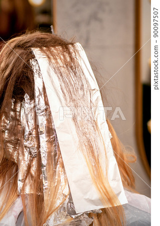 Beautiful young caucasian woman with foil in her hair while dyeing her hair sitting in a beauty salon 90097507