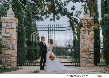 Happy stylish smiling couple walking in Tuscany, Italy on their wedding day. The bride and groom walk down the street by the hands. A stylish young couple walks. Husband and wife communicate nicely 90098705