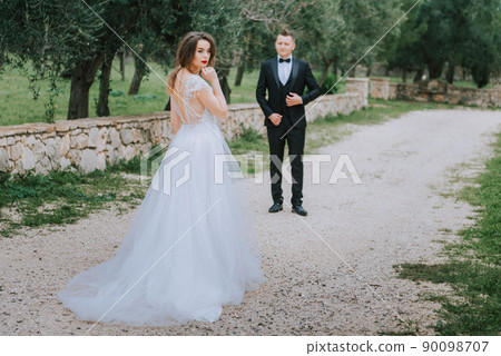 Happy stylish smiling couple walking in Tuscany, Italy on their wedding day. The bride and groom walk down the street by the hands. A stylish young couple walks. Husband and wife communicate nicely Happy stylish smiling couple walking in Tuscany, Italy on their wedding day. The bride and groom walk down the street by the hands. A stylish young couple walks. Husband and wife communicate nicely 90098707