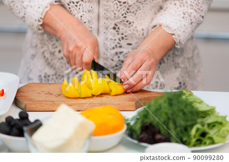 An elderly woman slices yellow bell peppers on a cutting board, close-up An elderly woman slices yellow bell peppers on a cutting board, close-up 90099280