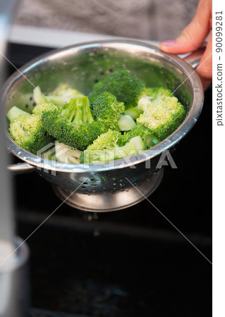 Washing broccoli in a colander in a black sink, close-up Washing broccoli in a colander in a black sink, close-up 90099281