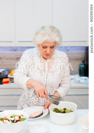 Grandma spreads healthy food on plates of steamed red fish and broccoli Grandma spreads healthy food on plates of steamed red fish and broccoli 90099364