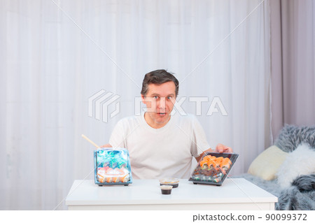 An elderly Caucasian man writhes funny faces, looking at sushi from a delivery 90099372