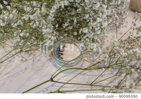 Candles made of soy wax with lavender in jars against the background of flowering gypsophila Candles made of soy wax with lavender in jars against the background of flowering gypsophila 90099390