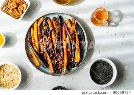 Roasted glazed spicy violet and orange carrots with ingredients on grey background. Top view 90099724