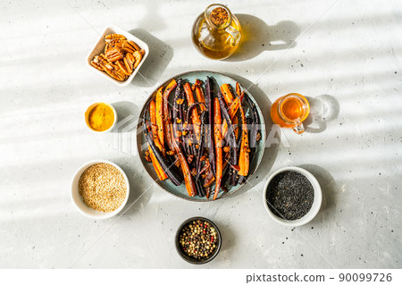 Roasted glazed spicy violet and orange carrots with ingredients on grey background. Top view Roasted glazed spicy violet and orange carrots with ingredients on grey background. Top view 90099726