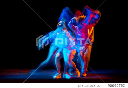 Young man and woman dancing hip-hop in sportive style clothes on dark background at dance hall in mixed neon light. Youth culture, hip-hop, movement Young man and woman dancing hip-hop in sportive style clothes on dark background at dance hall in mixed neon light. Youth culture, hip-hop, movement 90099762