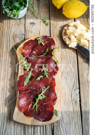 Jerky meat bresaola with lemons, grana and arugula Jerky meat bresaola with lemons, grana and arugula 90099786