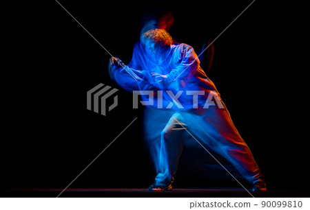 Young sportive man dancing hip-hop in sportive style clothes isolated on dark background at dance hall in mixed neon light. Youth culture, hip-hop, movement 90099810
