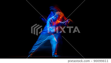 Astonished man, hip-hop dancer in sportive style clothes dancing isolated on dark background at dance hall in mixed neon light. Youth culture, hip-hop, movement 90099811
