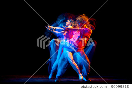 Dynamic portrait of stylish man and girl dancing hip-hop in sportive style clothes on dark background at dance hall in mixed neon light. Youth culture, breakdance, movement Dynamic portrait of stylish man and girl dancing hip-hop in sportive style clothes on dark background at dance hall in mixed neon light. Youth culture, breakdance, movement 90099818