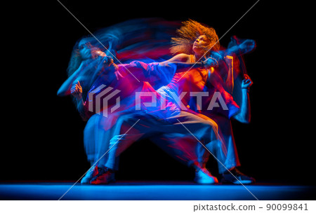Young man and woman dancing hip-hop in sportive style clothes on dark background at dance hall in mixed neon light. Youth culture, hip-hop, movement Young man and woman dancing hip-hop in sportive style clothes on dark background at dance hall in mixed neon light. Youth culture, hip-hop, movement 90099841