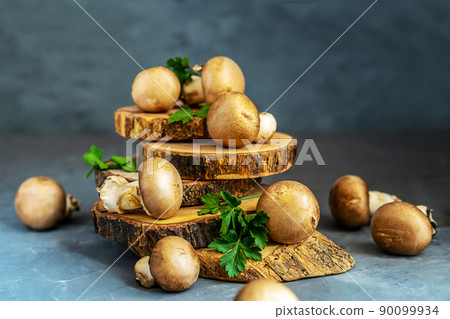 Raw mushrooms champignons with parsley on grey background Raw mushrooms champignons with parsley on grey background 90099934