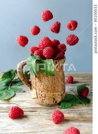 Flying raspberries under corkwood cup on the wooden table with fresh leaves Flying raspberries under corkwood cup on the wooden table with fresh leaves 90100033